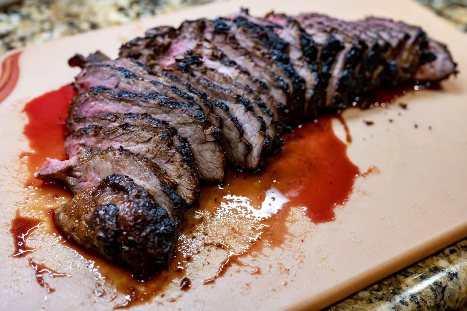 Sliced grilled steak with juices on cutting board