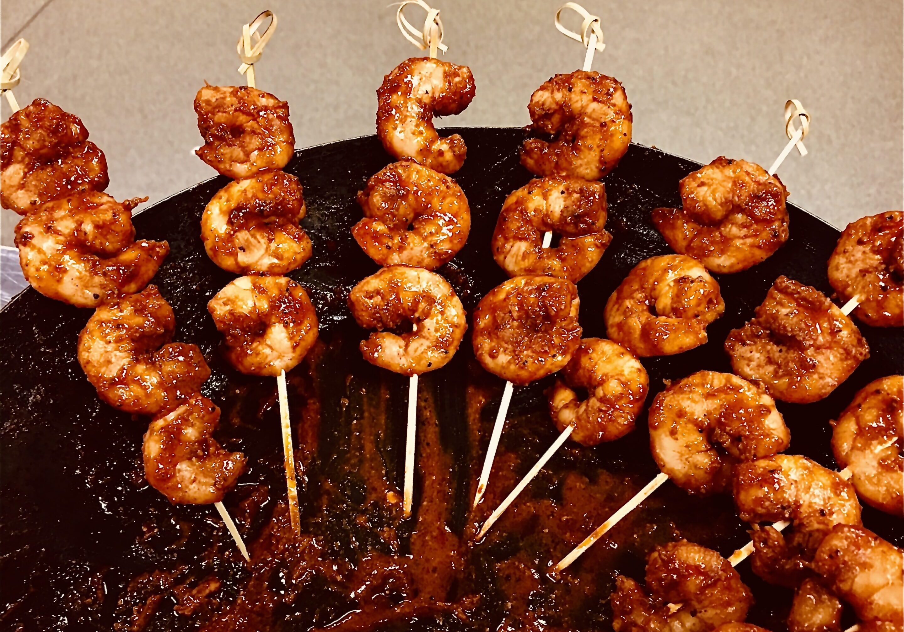 Glazed grilled shrimp skewers on black platter