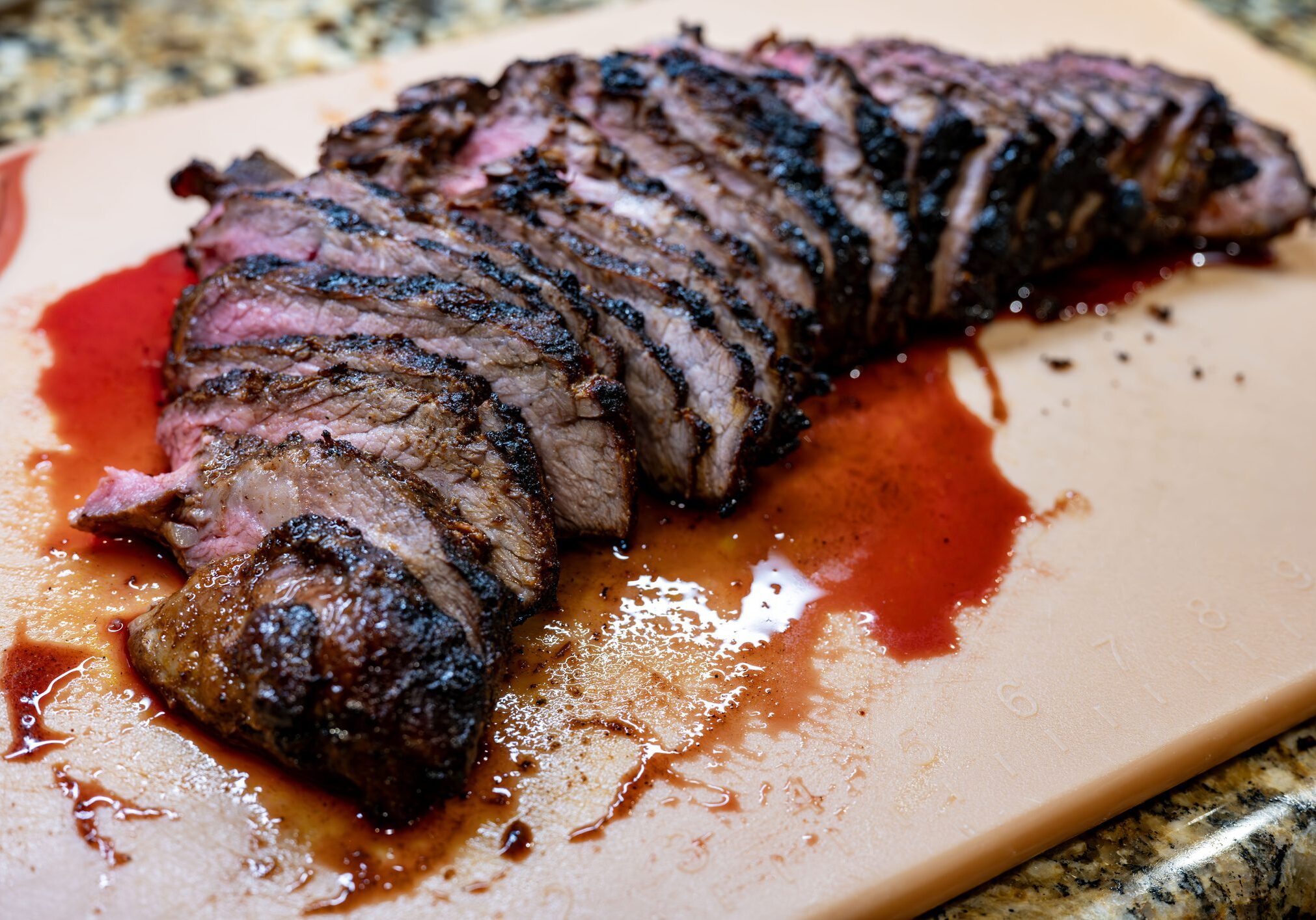 Sliced grilled steak with juices on cutting board